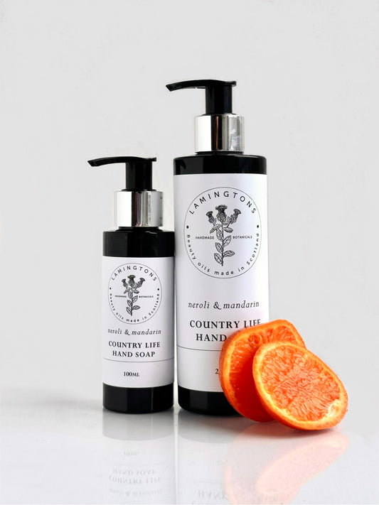Two bottles of Country Life Hand Soap: Neroli & Mandarin, pictured with an orange on a neutral background.